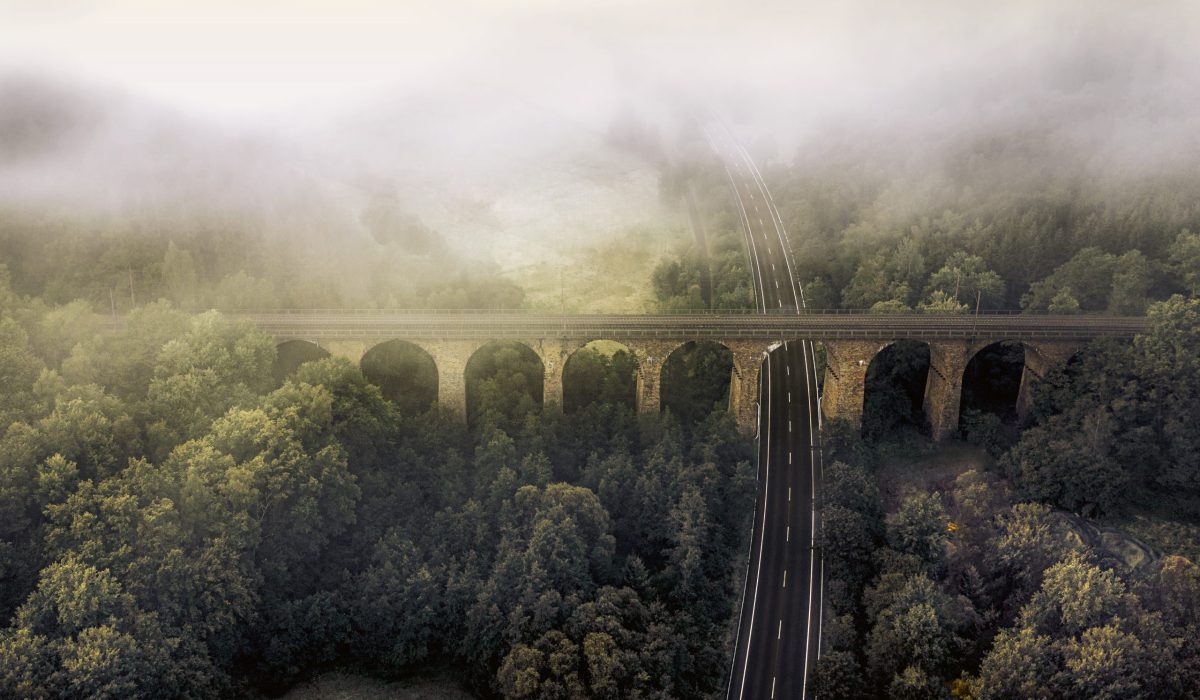 An aerial view shot of a road surrounded by greenery and clouds