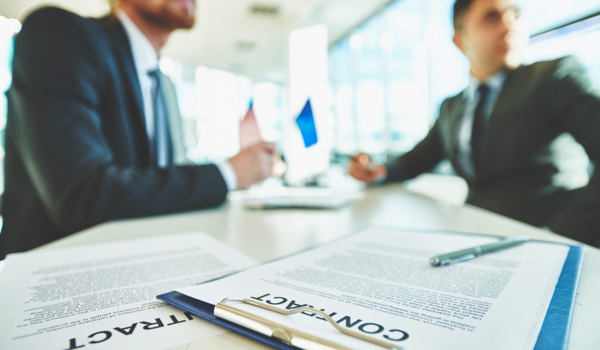 Business contracts on the desk with two male colleagues sitting on background